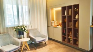 A room with two armchairs, a small table, a potted plant, and a shelf with decorative items.