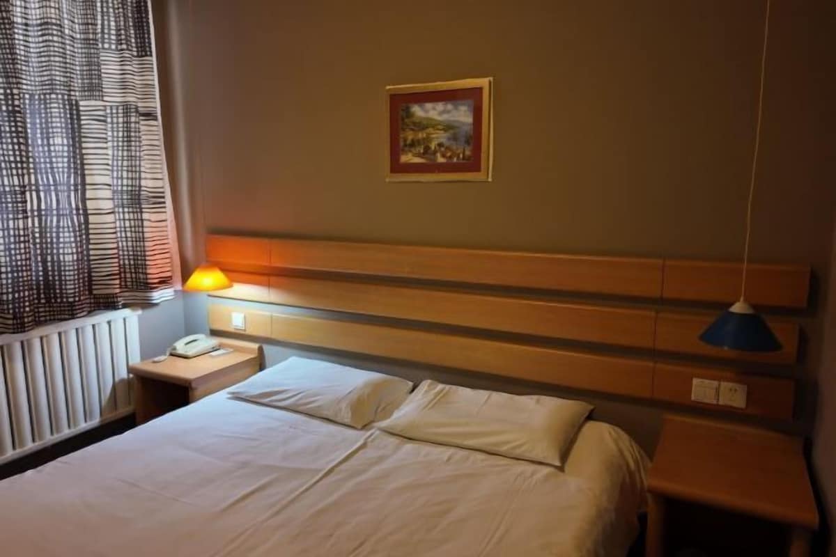 A hotel room with a bed, bedside table, lamp, and a painting on the wall.