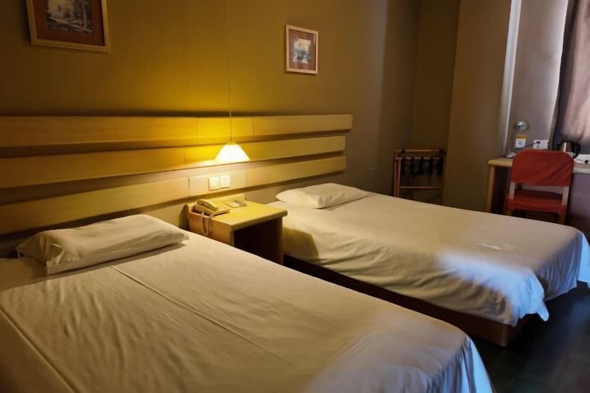 A hotel room with two beds, a bedside table with a lamp, a chair, and a desk with a telephone.