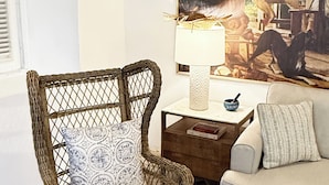 A wicker chair with a patterned cushion, a small table with a lamp, a bowl, and a couch with a pillow. - The Sunny Patio Oasis (San Juan)