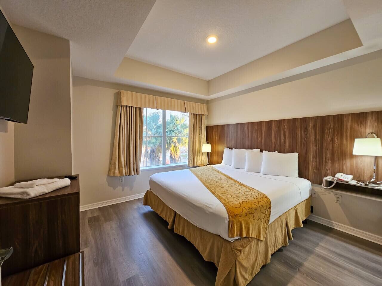 Una habitación de hotel con una cama grande, una mesita de noche, una lámpara y una ventana con cortinas.