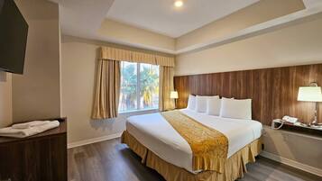 Una habitación de hotel con una cama grande, una mesita de noche, una lámpara y una ventana con cortinas.