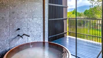 Un espace spa comprenant un jacuzzi, un mur en béton et une vue sur un jardin, séparé par une paroi en verre.