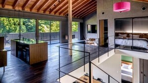 Un interno moderno con soffitto alto, ampie finestre, isola centrale e un letto al piano superiore.