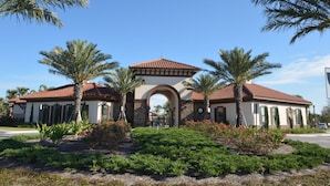 A two-story building with a red-tiled roof, an arched entrance, and palm trees in the foreground. - Lovely Home in Gated Resort with Extensive Amenities (Davenport)