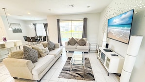 A modern living room with a sofa, coffee table, TV, and a dining area with chairs and a table. - Lovely Home in Gated Resort with Extensive Amenities (Davenport)