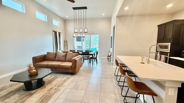 A spacious living area with a sofa, coffee table, and dining table. There is a kitchen with a bar area and a ceiling fan. - Modern 4BR, 3 King Beds + Full Near Red Hawk (Las Cruces)