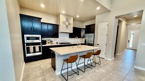 A modern kitchen with dark cabinets, a central island with bar stools, and a stainless steel refrigerator. - Modern 4BR, 3 King Beds + Full Near Red Hawk (Las Cruces)