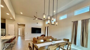 A modern dining area with a wooden table and chairs, a ceiling fan, recessed lighting, and a flat-screen TV mounted on the wall. - Modern 4BR, 3 King Beds + Full Near Red Hawk (Las Cruces)
