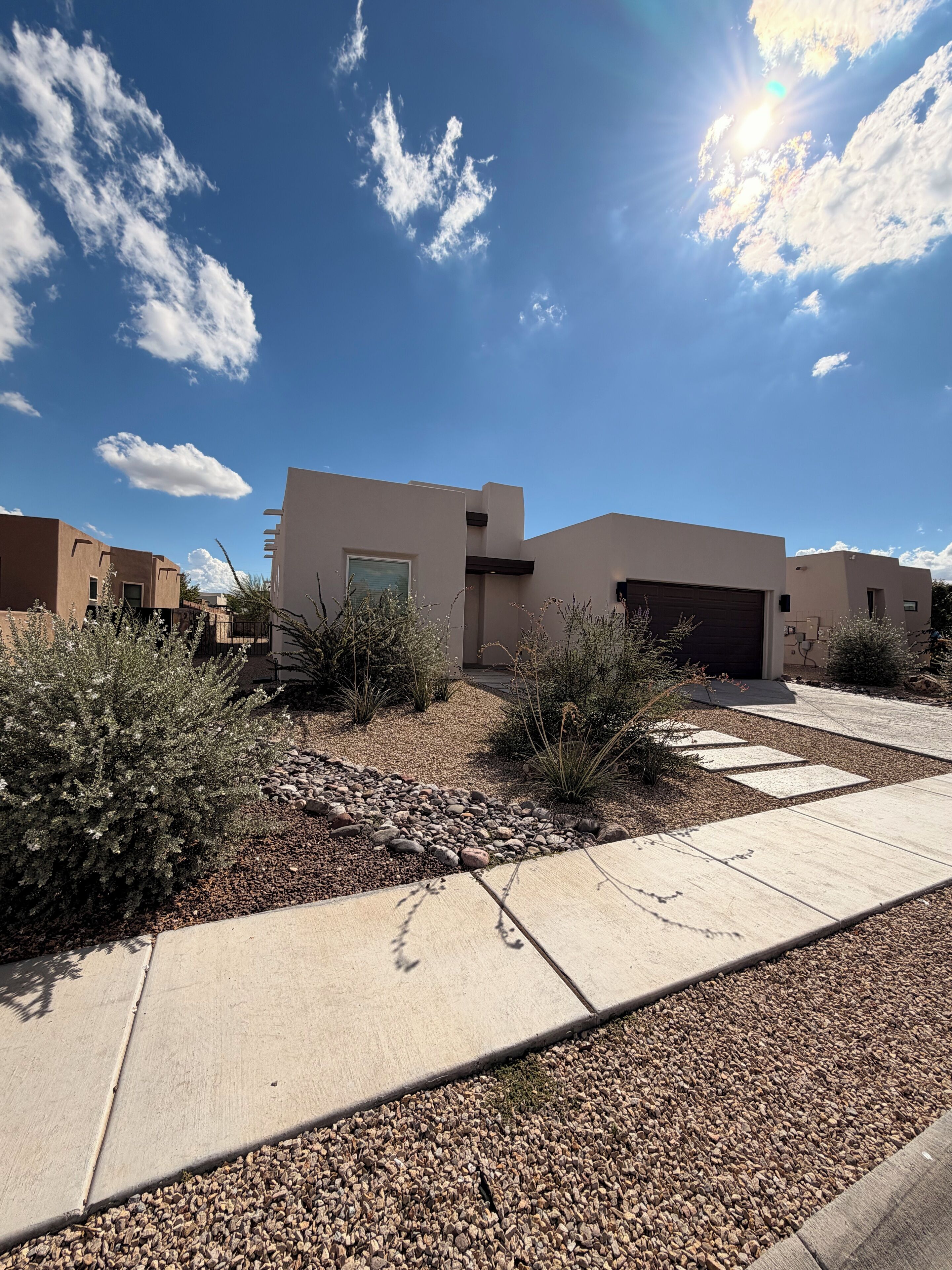 A modern house with a garage, surrounded by a gravel driveway and desert plants.