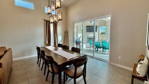 A dining area with a long wooden table, multiple chairs, and a hanging light fixture. - Modern 4BR, 3 King Beds + Full Near Red Hawk (Las Cruces)