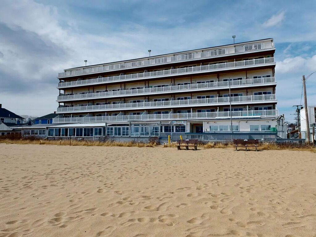 A multi-story hotel with balconies, located on a sandy beach.
