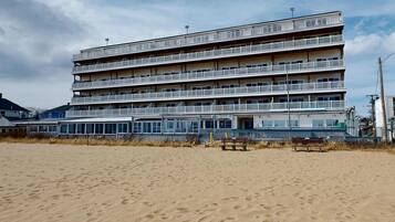 A multi-story hotel with balconies, located on a sandy beach.