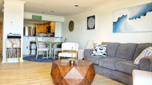 A living room with a grey sofa, a round wooden coffee table, and a dining area with wooden cabinets and a white table. - The Brunswick Penthouse with Panoramic Oceanfront Balconies-2 bedroom/2.5 bath (Old Orchard Beach)