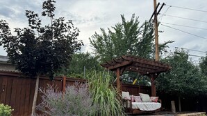 A wooden pergola with a swing bed, surrounded by various plants and a wooden fence. - Spacious Luxury Retreat, Fireplace, Garden Oasis (Denver)