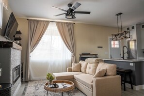 A living room with a sofa, a coffee table, a fireplace, and a kitchen area with a refrigerator.