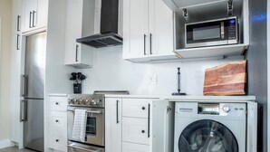 A modern kitchen with white cabinetry, stainless steel appliances, a microwave, and a built-in washer and dryer. - Spacious Luxury Retreat, Fireplace, Garden Oasis (Denver)