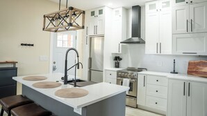 A modern kitchen with white cabinetry, a central island with stools, a stainless steel stove, and a hanging light fixture. - Spacious Luxury Retreat, Fireplace, Garden Oasis (Denver)
