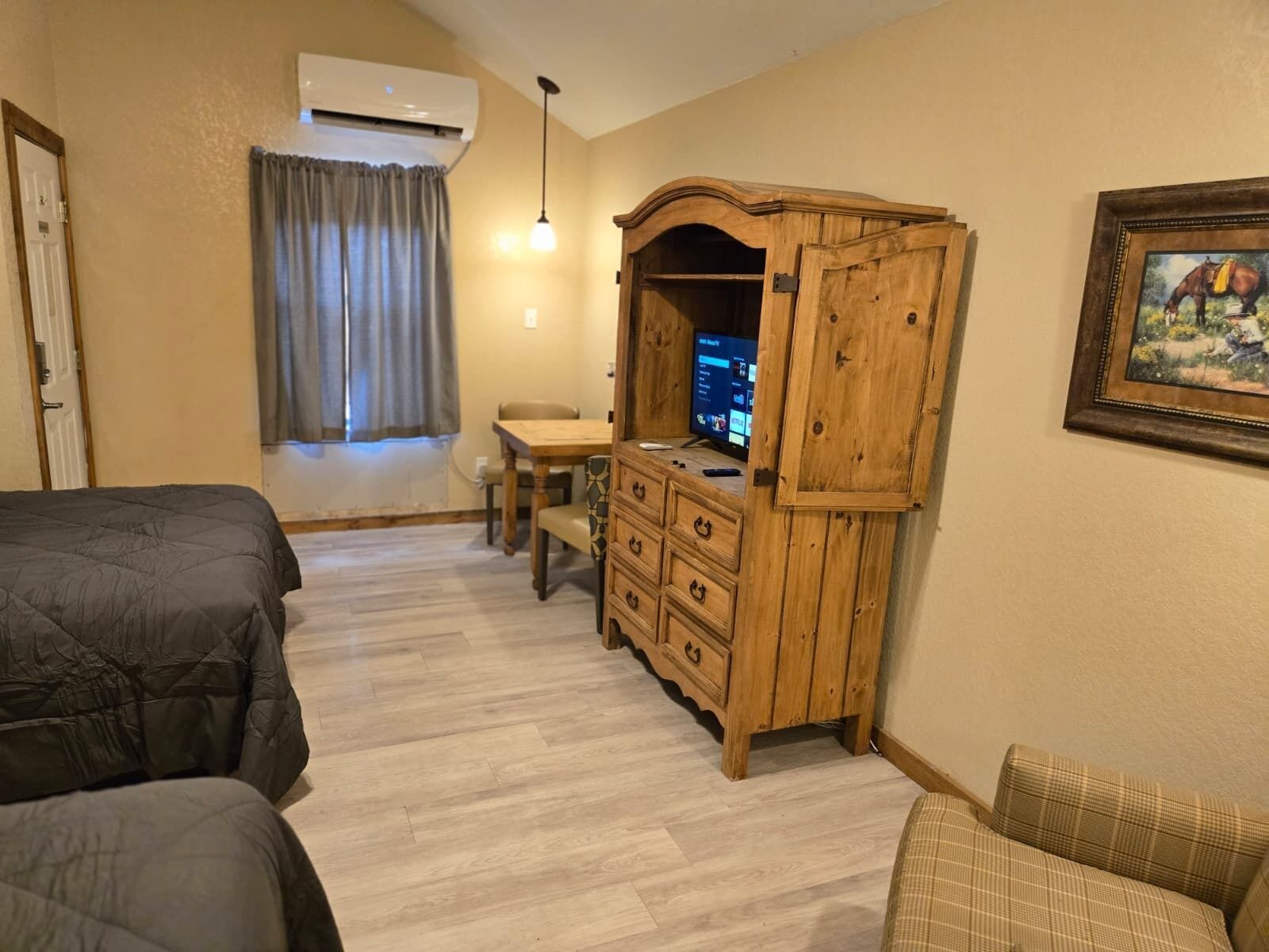 A room with two beds, a wooden dresser with a TV, a window with curtains, and a painting on the wall.