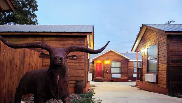 Un bâtiment rustique, avec une grande statue de taureau devant, un revêtement extérieur en bois et une porte rouge.