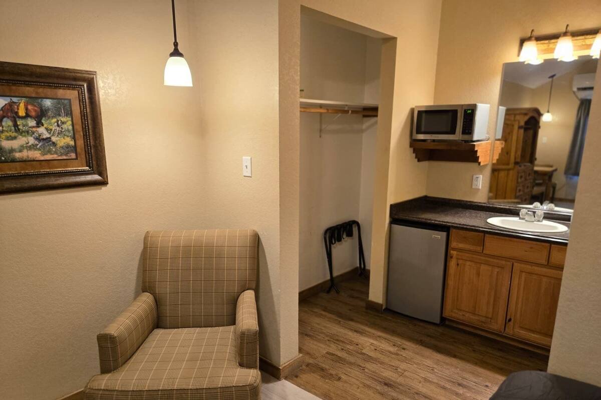 A small, cozy room with a plaid armchair, a compact kitchenette with a microwave, and a wooden floor.