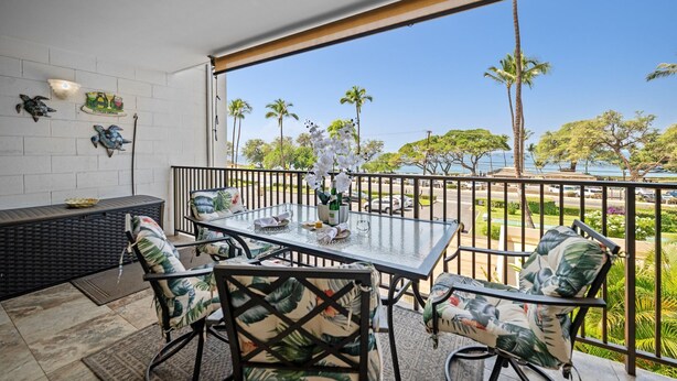 Ein Balkon mit Glastisch und Stühlen, Blick auf Palmen und eine weiße Wand mit Dekorationselementen.