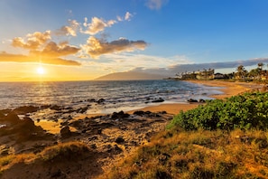A coastal landscape with a beach, rocky shoreline, and vegetation. - Direct Ocean Views, Private Lanai (Kihei)