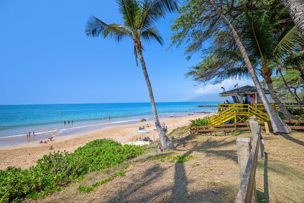A beach with palm trees, a lifeguard tower, and a sandy shore with people. - Direct Ocean Views, Private Lanai (Kihei)