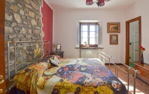 Quarto com parede de pedra, cama com colcha colorida, janela com vista e radiador.