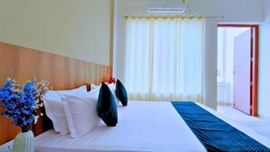 A hotel room with a large bed, a wooden headboard, white bedding, and a blue accent on the floor. - Foreste Resort (Ramnagar)