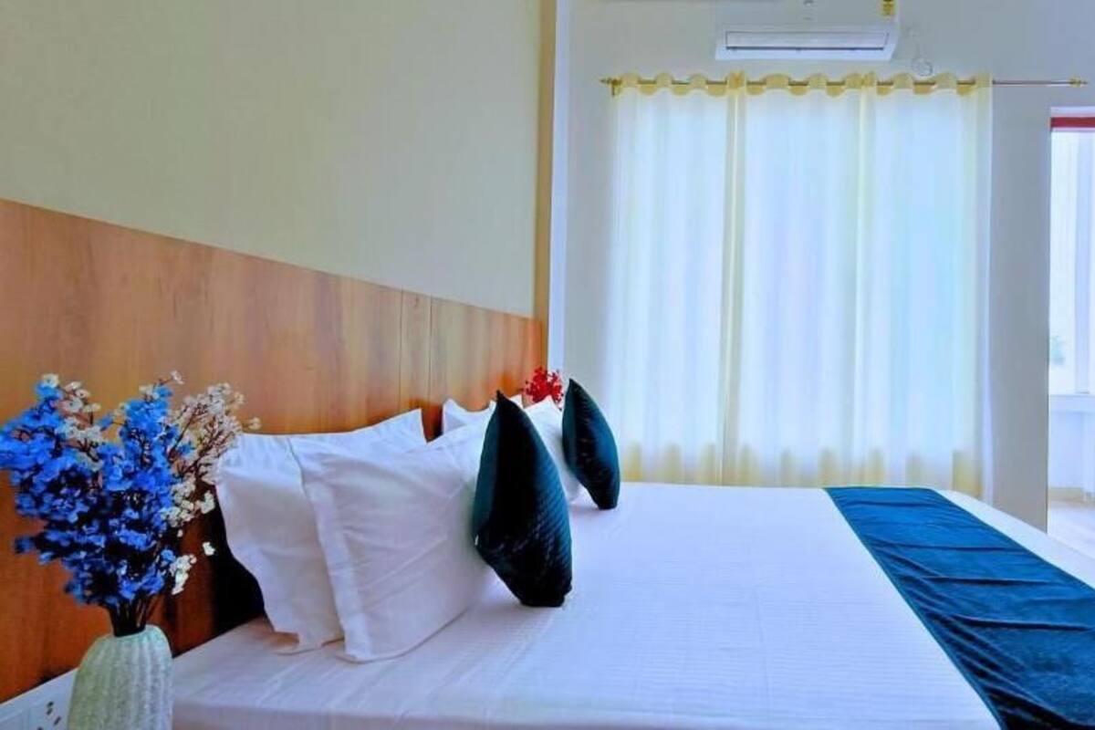 Quarto de hotel com uma cama grande, cabeceira de madeira, roupa de cama branca e um toque de azul no chão.