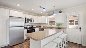 A modern kitchen with white cabinets, stainless steel appliances, a granite countertop, and a bar stool area. - Little Island Time: Walk to Beach Retreat (Kitty Hawk)
