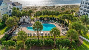 Een resort met een zwembad, omringd door palmbomen en ligstoelen, met uitzicht op een strand en de oceaan.