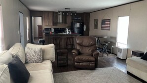 Una sala de estar con un sofá, un sillón de cuero y una cocina al fondo.