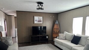 Una sala de estar con un sofá, un televisor, un estante de madera y una alfombra estampada.