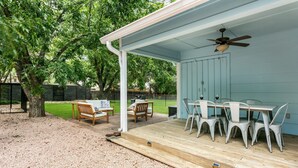 A covered outdoor patio with a table and chairs, a ceiling fan, and a view of a grassy yard. - Dogologie Haus | 2/2, Pet Amenities, Gas Grill, Pets w/ Fee (Fredericksburg)