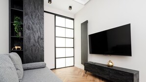 A modern living room with a grey sofa, a black entertainment unit, and a large flat-screen TV mounted on the wall. - Piotrkowska Grand Avenue Apartment #C (Łódź)