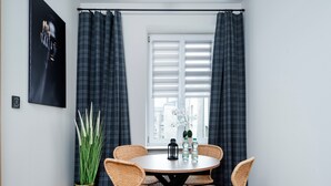 A dining area with a round table, four wicker chairs, a potted plant, and a window with curtains.