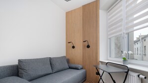 A modern living room with a grey sofa, wooden panel wall, and a window with blinds.