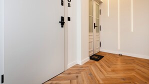 A hallway with a wooden herringbone floor, white walls, and doors marked with '9B'.