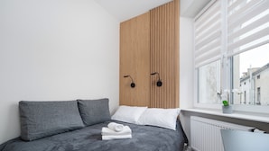 A modern bedroom with a grey bed, white pillows, a wooden panel wall, and a window with a view of buildings.