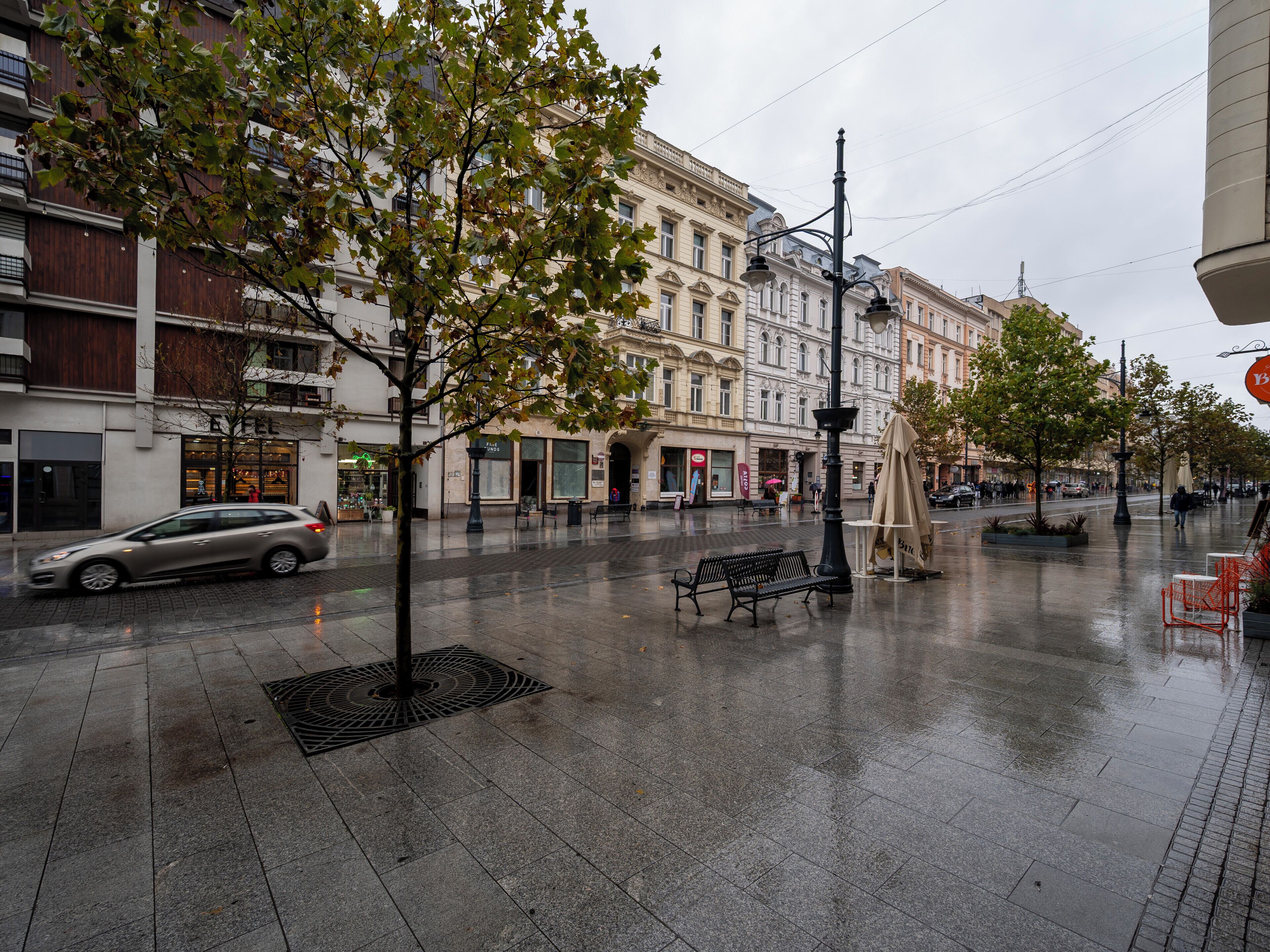 Een nat stadsplein met banken, bomen en gebouwen.