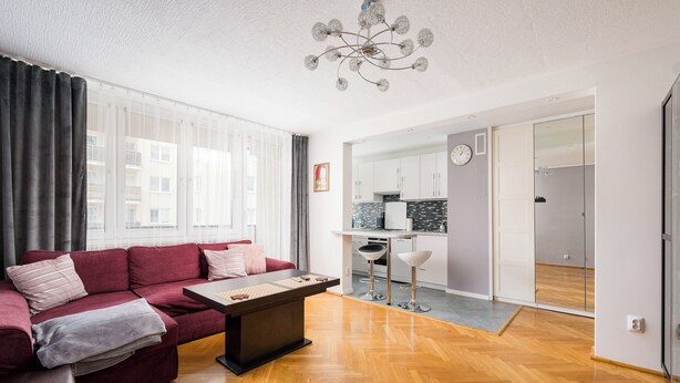 A modern living room with a sofa, a coffee table, and a dining area with a kitchen in the background. - Warszawa Wola Homely Apartment (Warszawa)