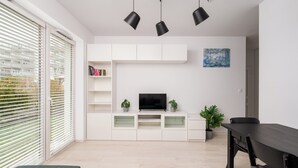 A modern living room with a flat-screen TV, white cabinetry, and a dining table.