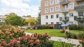A modern apartment building with balconies, a garden area with pink flowers, and a pathway.