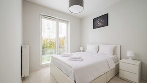 A bedroom with a bed, bedside tables, a radiator, and a window with blinds.