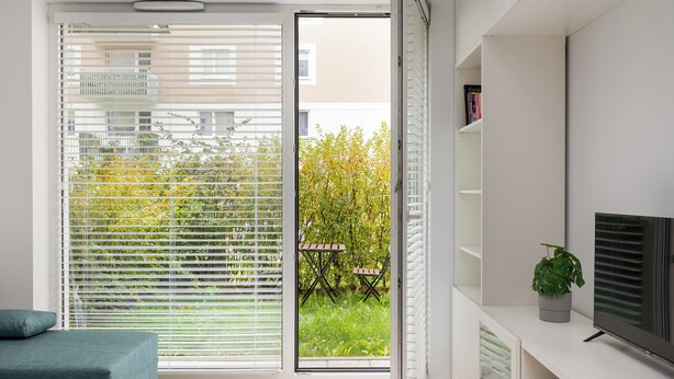 A modern living room with a sliding glass door leading to a balcony, a flat-screen TV, and a small potted plant.