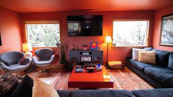 Una sala de estar con una televisión de pantalla plana, dos sillones, un sofá, una mesa de centro y una estantería.