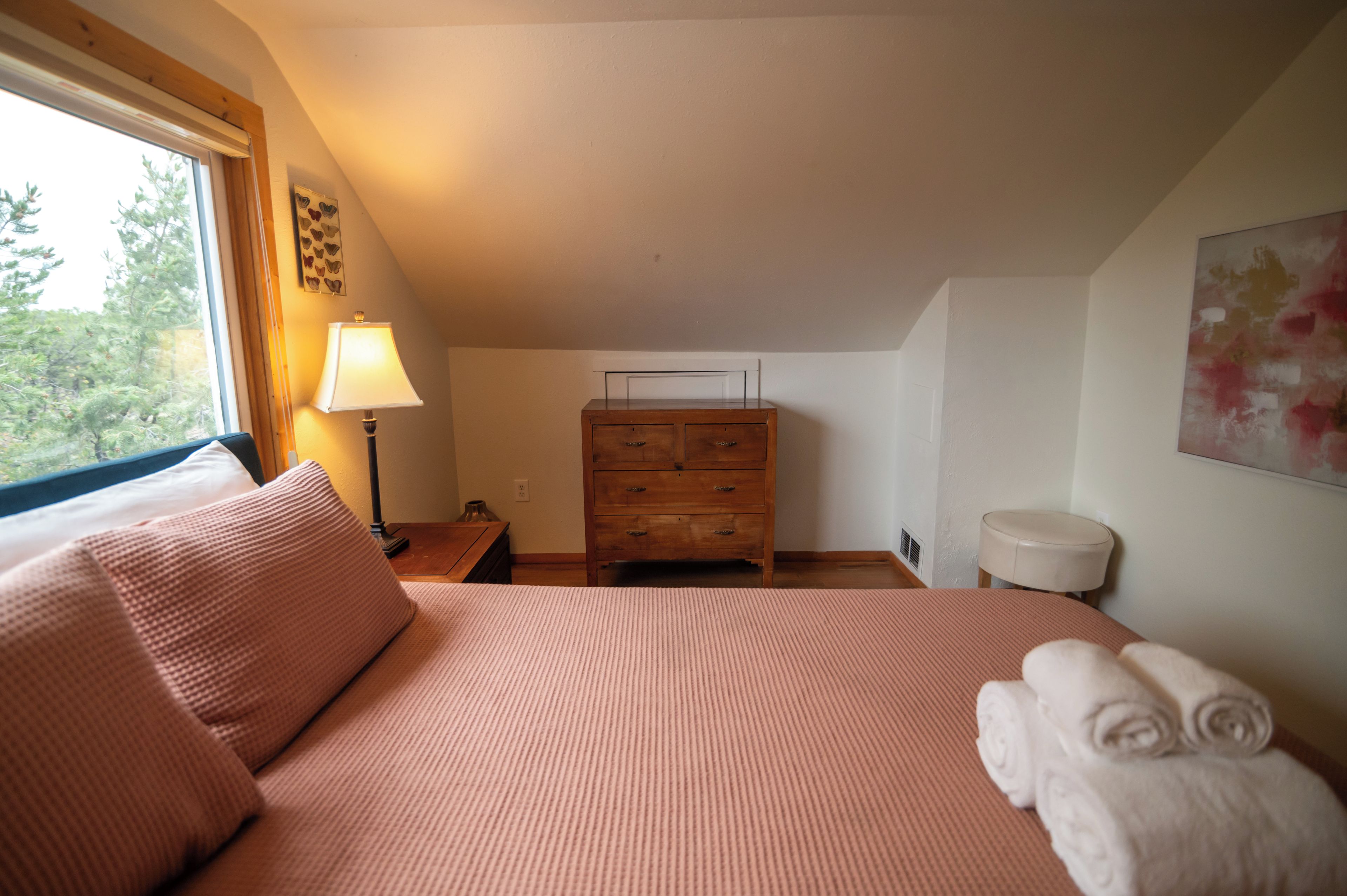 A bedroom with a bed, a wooden dresser, a nightstand, and a lamp.