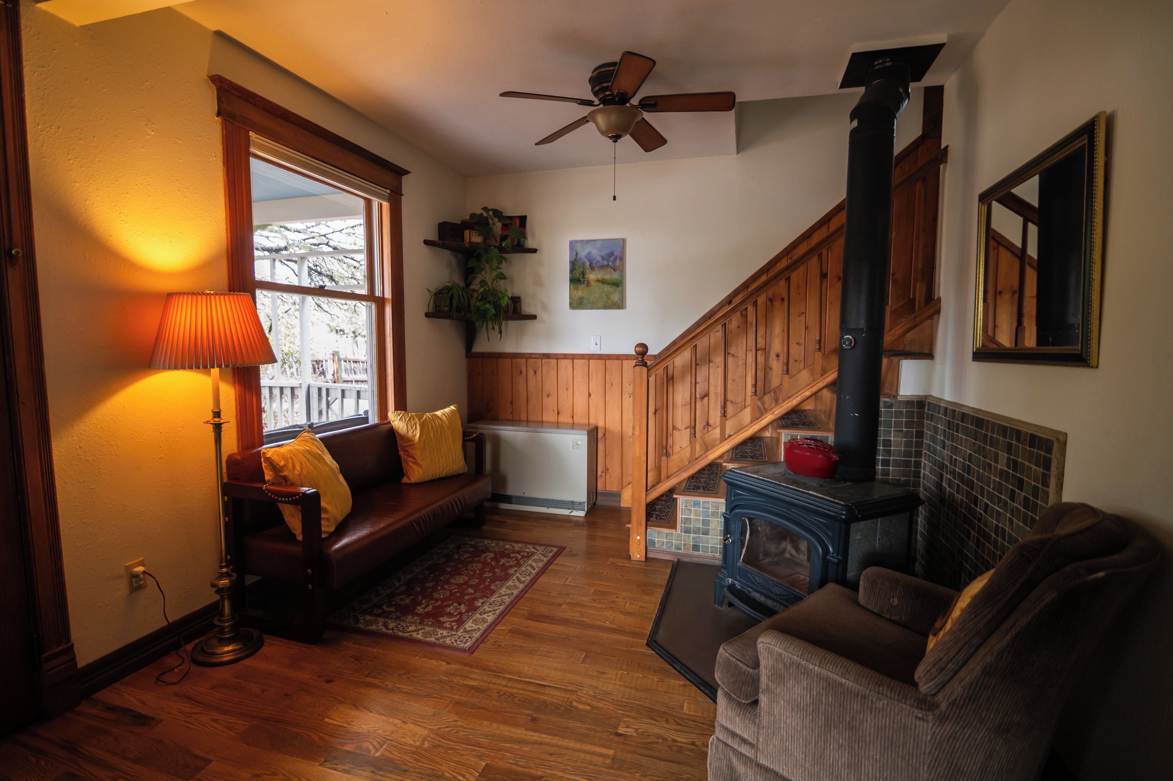 A cozy living room with a wooden floor, a sofa, a lamp, a fireplace, and a staircase.